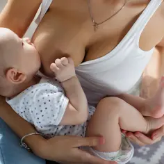Ciepły moment karmienia piersią. 3 miesięczne dziecko z zaciekawieniem spogląda na świat, ssąc mleko mamy.